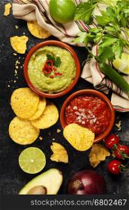 Green Homemade Guacamole with Tortilla Chips and Salsa on dark rustic background.