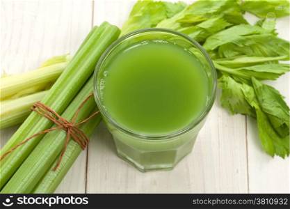 Green juice with celery stalk on white wood
