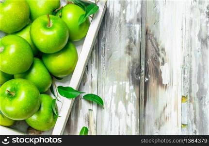Green juicy whole apples in a wooden box. On a white wooden background.. Green juicy whole apples in a wooden box.