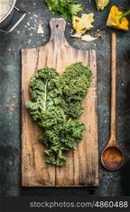 Green kale leaves on rustic cutting board with wooden cooking spoon , top view