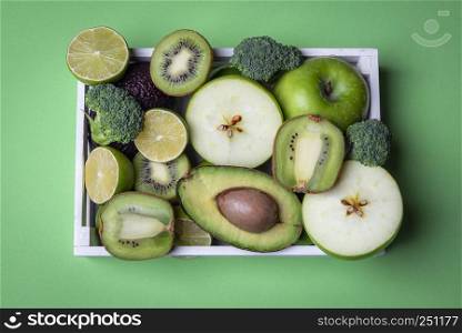 Green kitchen table above view with many fresh fruits and vegetables in a wooden tray. Directly above view with copy space