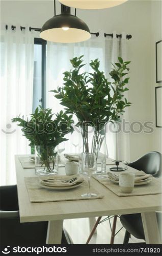 Green leaves in vase at center of simply dining table with vintage pendant