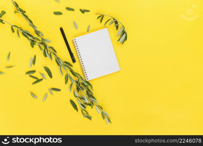 green leaves with pen spiral blank notepad yellow background