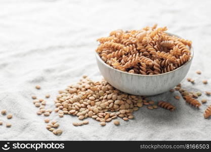 Green lentil fusilli pasta on a gray textile background. A bowl of raw pasta and green lentils. Gluten-free pasta.