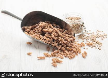 Green lentil fusilli pasta on a wooden background. A scoop of raw pasta and green lentils. Gluten-free pasta.