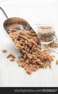 Green lentil fusilli pasta on a wooden background. A scoop of raw pasta and green lentils. Gluten-free pasta.