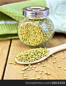 Green lentils in a glass jar and a wooden spoon, napkin on the background of wooden boards