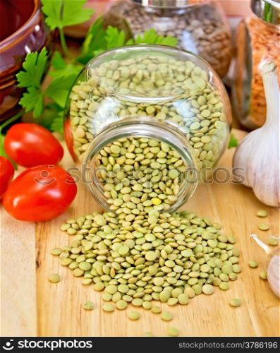 Green lentils in a glass jar, parsley, garlic, tomatoes, clay pot, napkin on the background of wooden boards