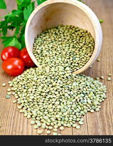 Green lentils in a wooden bowl with parsley and red tomatoes on a wooden boards background