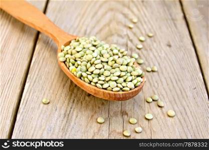 Green lentils in a wooden spoon on a wooden boards background