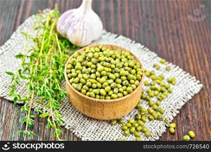 Green lentils mung in a wooden bowl with thyme and garlic on sackcloth, hot peppers on a wooden board background
