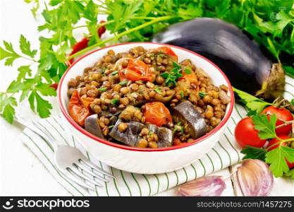 Green lentils stewed with eggplant, tomatoes, garlic and spices in a bowl on a napkin, parsley on wooden board background