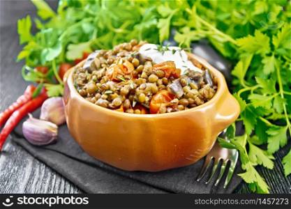 Green lentils stewed with eggplant, tomatoes, garlic and spices, sour cream sauce with a sprig of thyme in bowl on a napkin, parsley on dark wooden board
