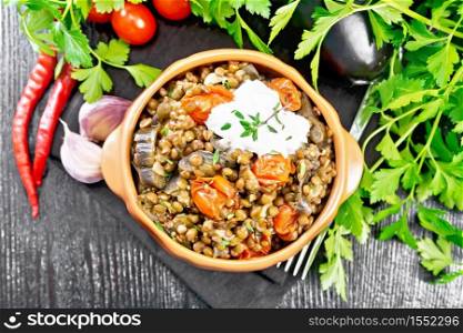 Green lentils stewed with eggplant, tomatoes, garlic and spices, sour cream sauce with a sprig of thyme in bowl on a towel, parsley on wooden board background from above