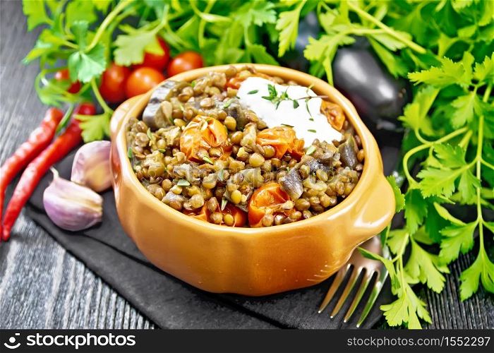Green lentils stewed with eggplant, tomatoes, garlic and spices, sour cream sauce with a sprig of thyme in a bowl on a towel, parsley on wooden board background