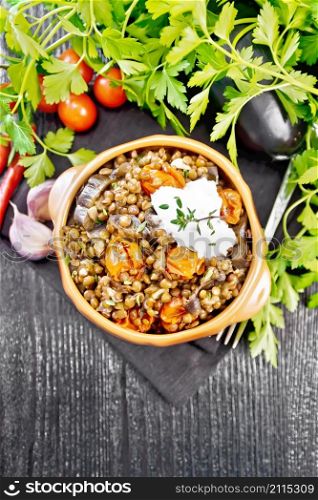 Green lentils stewed with eggplant, tomatoes, garlic and spices, sour cream sauce with sprig of thyme in a bowl on a napkin, parsley on dark wooden board from above