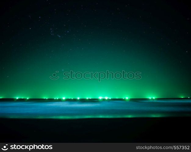 Green light at horizon line over the sea, light from fishing boat, star on the sky and soft movement of wave, Thailand
