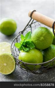 Green  Limes with fresh mint leaves in basket, concrete background