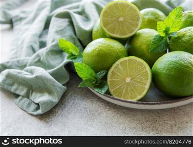 Green  Limes with fresh mint leaves on  plate, concrete background