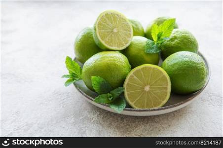 Green  Limes with fresh mint leaves on  plate, concrete background