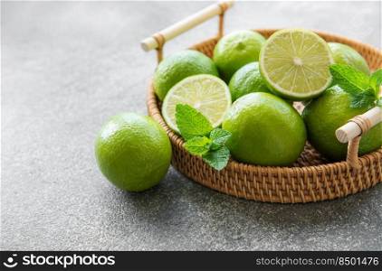 Green  Limes with fresh mint leaves on  wicker tray, concrete background