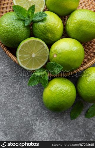 Green  Limes with fresh mint leaves on  wicker tray, concrete background