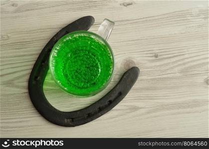 Green liquid in a beer mug displayed with a horseshoe for St. Patrick's day