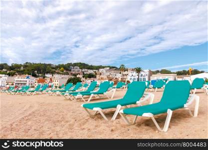 Green lounge chairs at the beach of Tossa de Mar in the early morning.