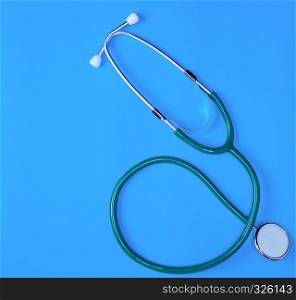 green medical stethoscope on blue background, close up, copy space