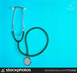 green medical stethoscope on blue background, close up, copy space