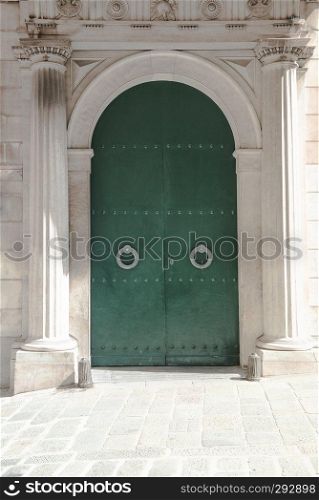 Green metal door fenced by two roman architecture columns. Historical building exterior on the streets of Genova, Italy
