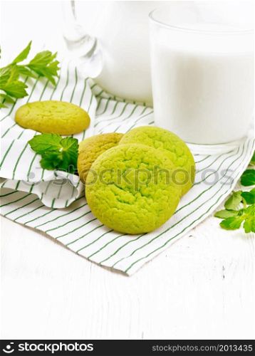 Green mint cookies on a napkin with milk in a glass on white wooden board background