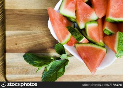 green mint flavored and sliced red and juicy watermelon on a wooden board, close-up of berries and plants. mint and watermelon