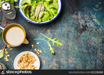 Green mix salad with oil dressing and pine nuts on rustic background, top view