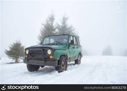 Green off-road vehicle on the snow-covered mountain in fog. Green off-road vehicle on the snow-covered mountain