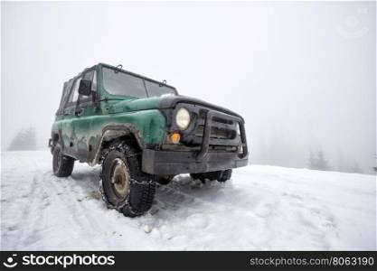 Green old off-road vehicle on the snow-covered mountain in fog. Green old off-road vehicle on the snow-covered mountain