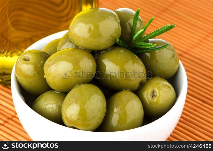 Green olives in a white ceramic bowl on orange background.