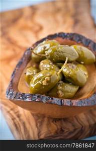 Green olives marinated with coriander in small wooden bowl over olive wood board, selective focus