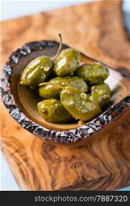 Green olives marinated with coriander in small wooden bowl over olive wood board, selective focus