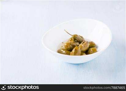 Green olives marinated with coriander in white bowl on light blue background, copy space, selective focus