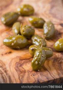 Green olives marinated with coriander over olive wood board, selective focus