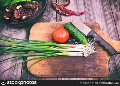 Green onions and fresh vegetables on a wooden cutting board, vintage toning