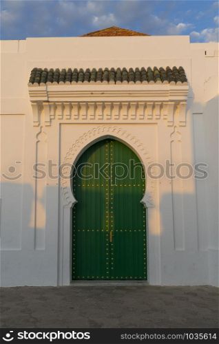 Green painted wooden door with gold colored decoration in the medina of Asilah, Morocco at setting sun