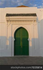 Green painted wooden door with gold colored decoration in the medina of Asilah, Morocco at setting sun