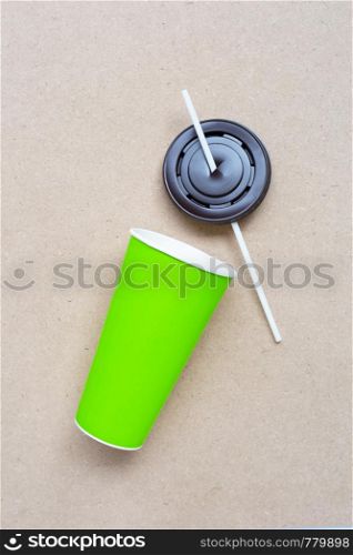 Green paper coffee cup with straw and plastic cap on plywood background.