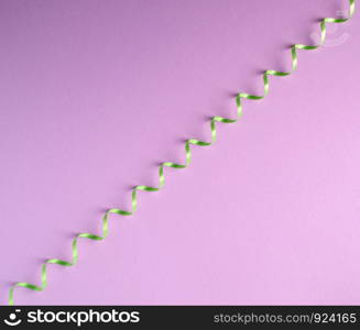 green paper serpentine on a lilac background, flat lay