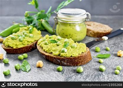 Green pea and chickpea hummus sandwiches, jar of dipping sauce, pea pods on granite countertop background