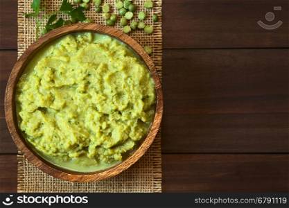 Green pea and parsley dip or spread in wooden bowl, photographed overhead on dark wood with natural light (Selective Focus, Focus on the top of the dip)
