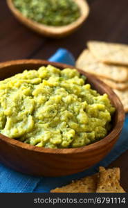 Green pea and parsley dip or spread in wooden bowl with soda crackers on the side, photographed with natural light (Selective Focus, Focus in the middle of the dip)