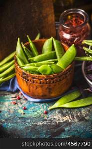 Green pea pods with cooking ingredients in bows on rustic kitchen table, top view